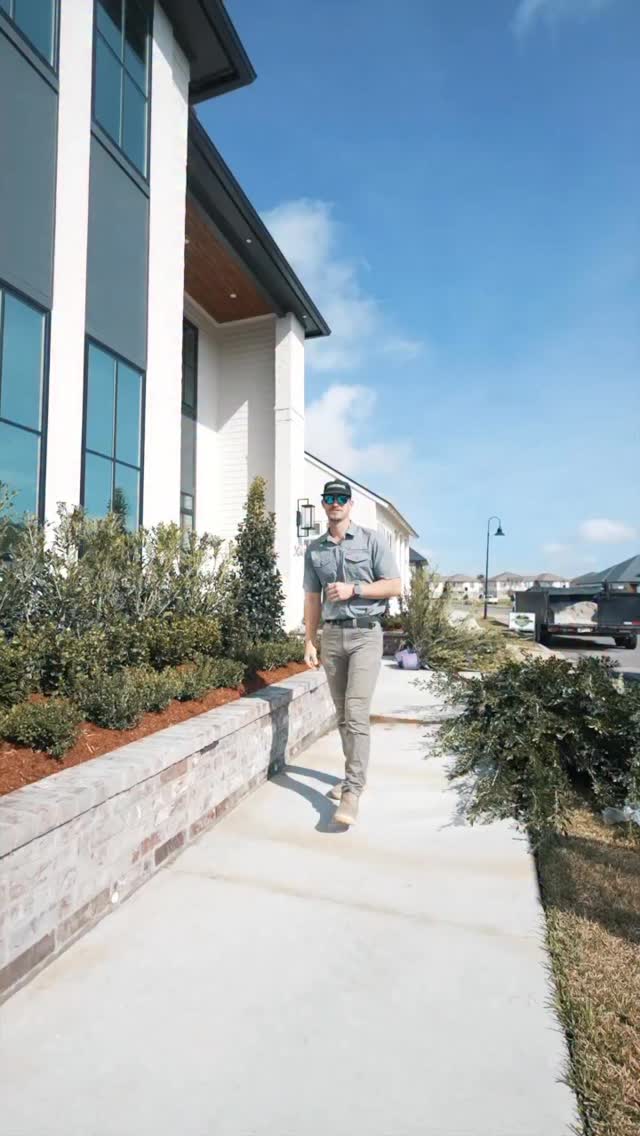 A presenter walks beside landscaped planting beds and a raised brick border outside a home.